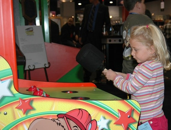 Child playing an arcade game with colorful machine and people in the background