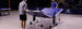 Two people setting up a portable ping pong table in an indoor setting with a visible brand logo.