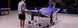 Two people setting up a portable ping pong table in an indoor setting with a visible brand logo.