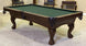 A traditional style pool table with arched cabinets, dentil holding side rails, and ball & claw legs in a dark finish, with green felt top and brown leather pockets.