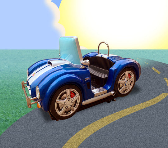 A blue and white toy model of a KC Cobra classic car positioned on a road with a grassy background and a sunny sky overhead.