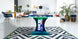 An ICE Super Chexx Bubble Hockey table with a blue base and red grips, featuring custom 40th graphics and LED lighting, placed in a modern room with plants and furniture around it.