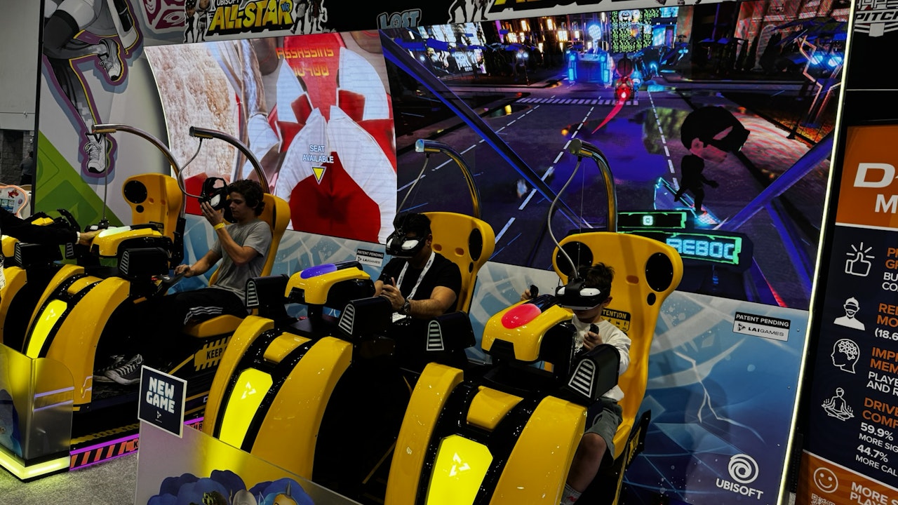 Simulator racing chairs in an arcade with video game displays on the wall.