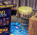 A yellow bar stool with a Pac-Man themed pattern, placed in front of an arcade machine featuring Namco classic games.