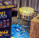 A yellow bar stool with a Pac-Man themed pattern, placed in front of an arcade machine featuring Namco classic games.