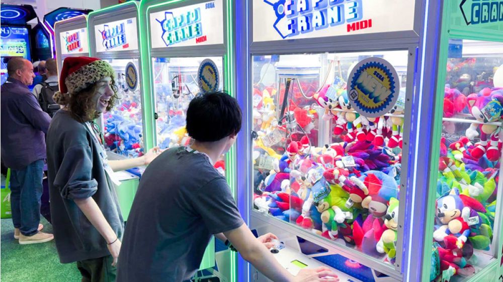 People playing claw machine games at an arcade with colorful prizes inside.