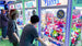 People playing claw machine games at an arcade with colorful prizes inside.