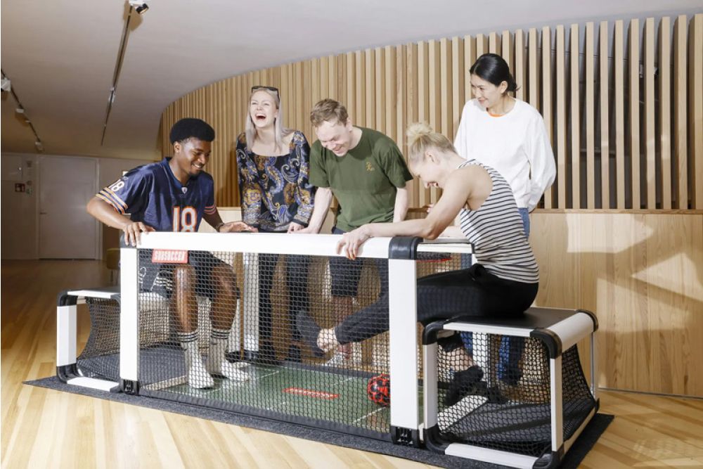 Group of people playing a game on a small sports court with a wooden wall background