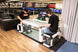 Two people playing air hockey in an indoor setting with various advertisements on the walls.